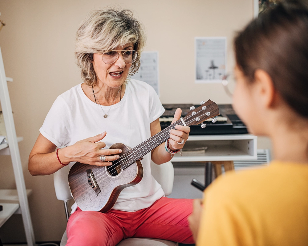 Woman teaching ukulele to a young girl.