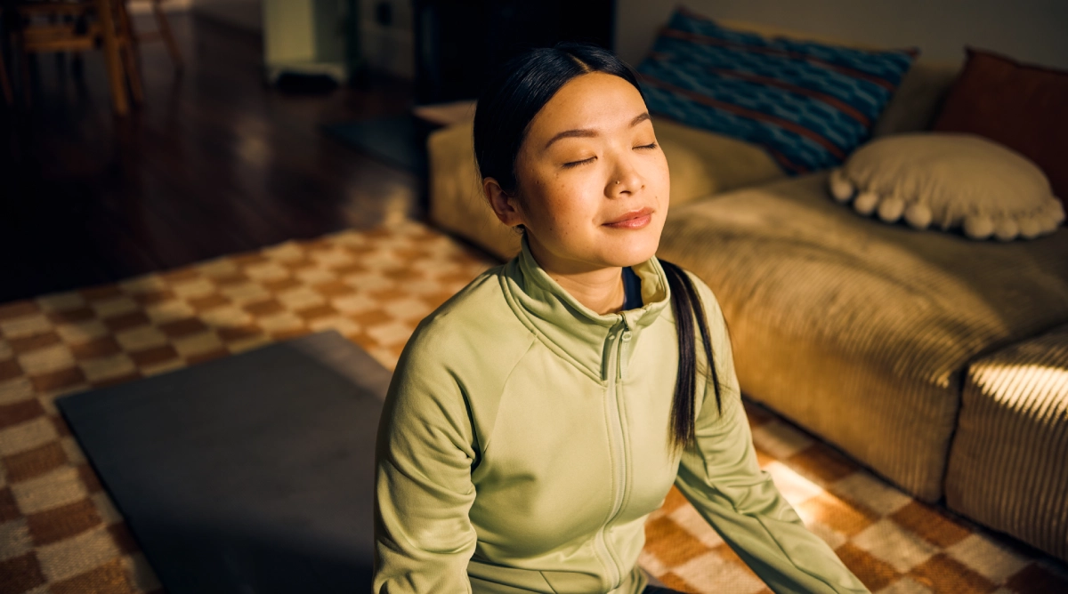 Woman meditating peacefully on living room floor.