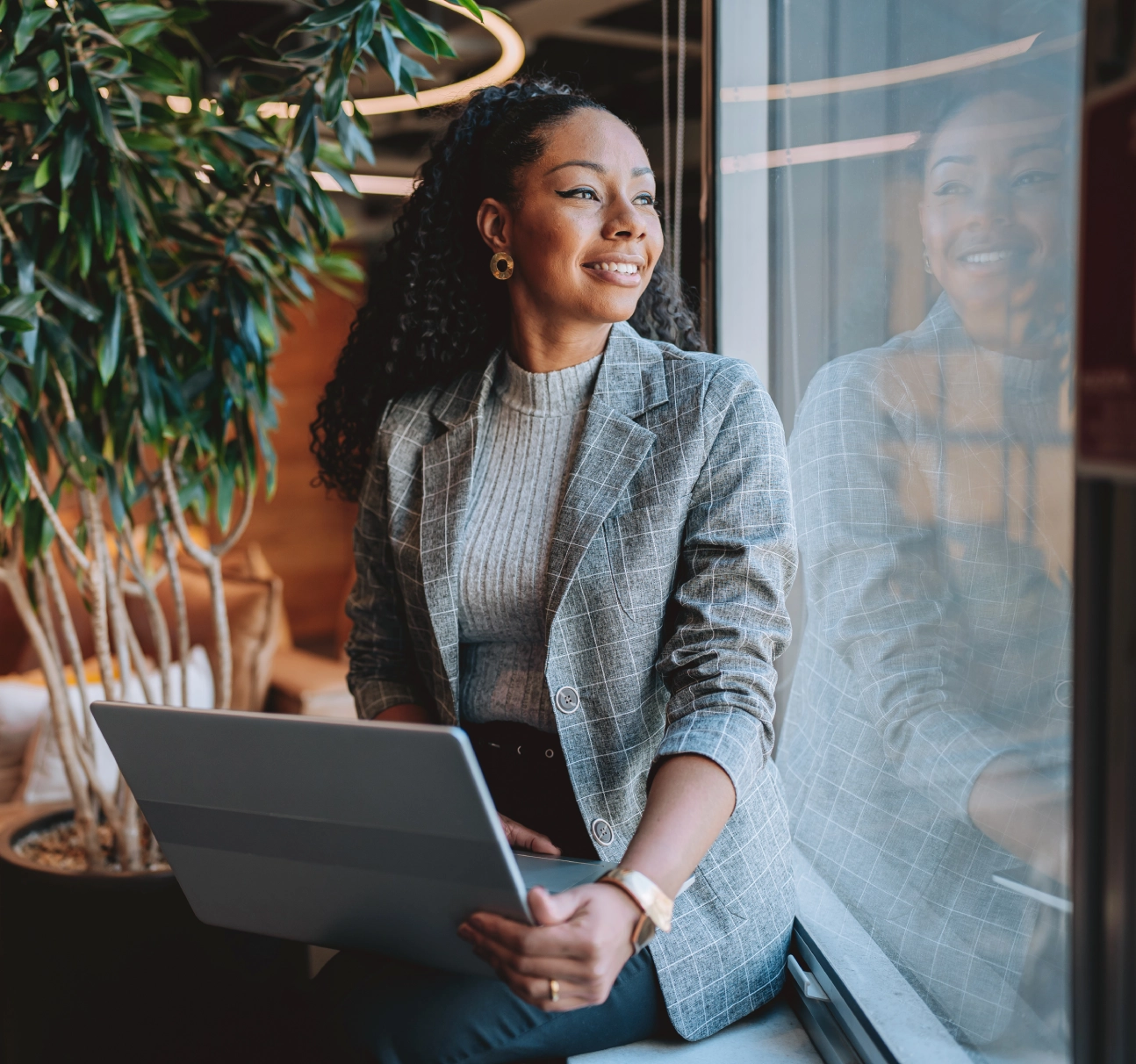 Woman smiling with laptop by window.
